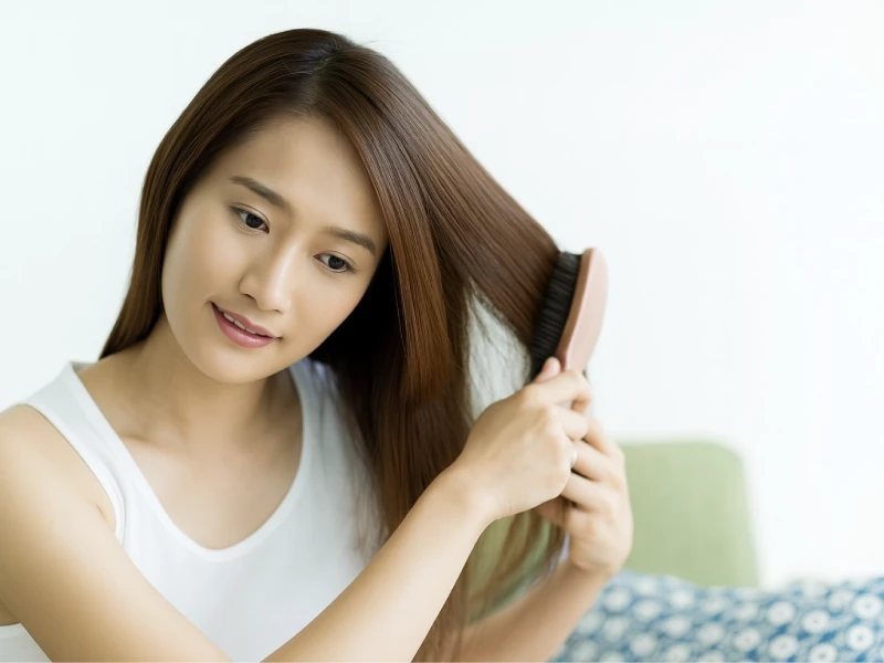 タンクトップを着て部屋で髪の毛をブラッシングしている女性