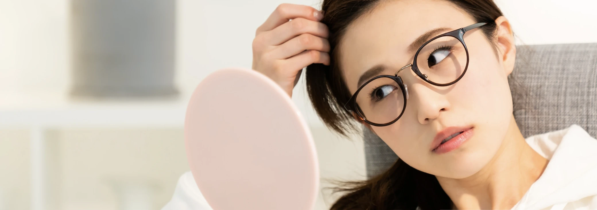 髪を触りながら手鏡に写った自分を見つめている眼鏡をかけた女性