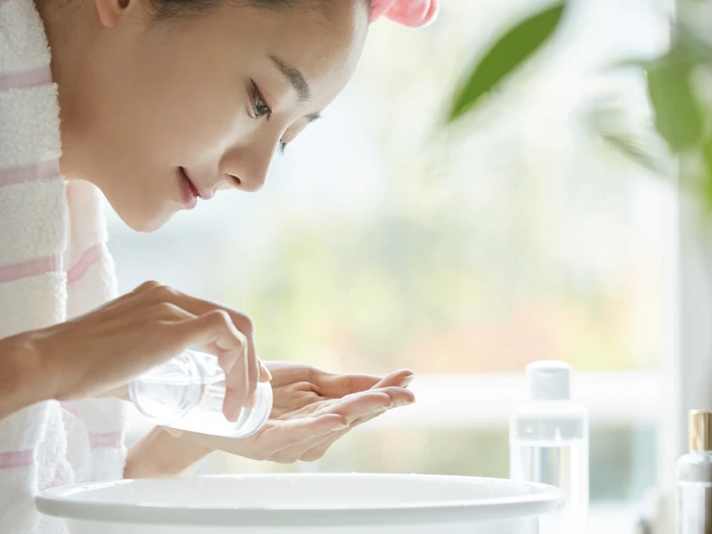 頭にタオルを巻き、洗面台で肌や髪のケアをする女性