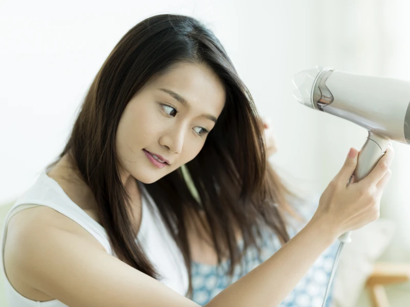 部屋で髪にドライヤーを当てている女性