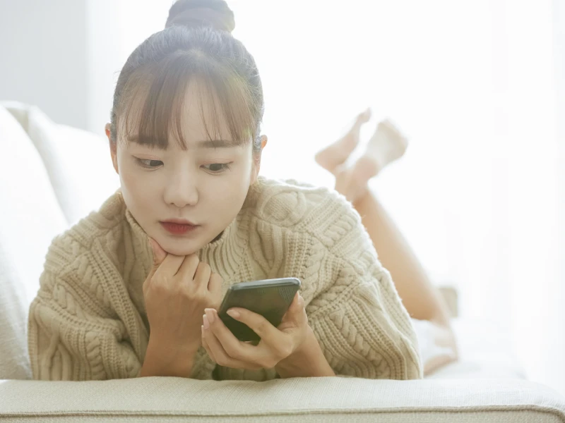 ソファーにうつ伏せになりながらスマホの画面を見ている女性