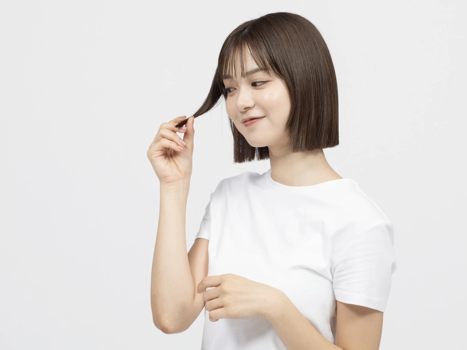 自分の毛先を指でつまんで髪のコンディションを確認している女性