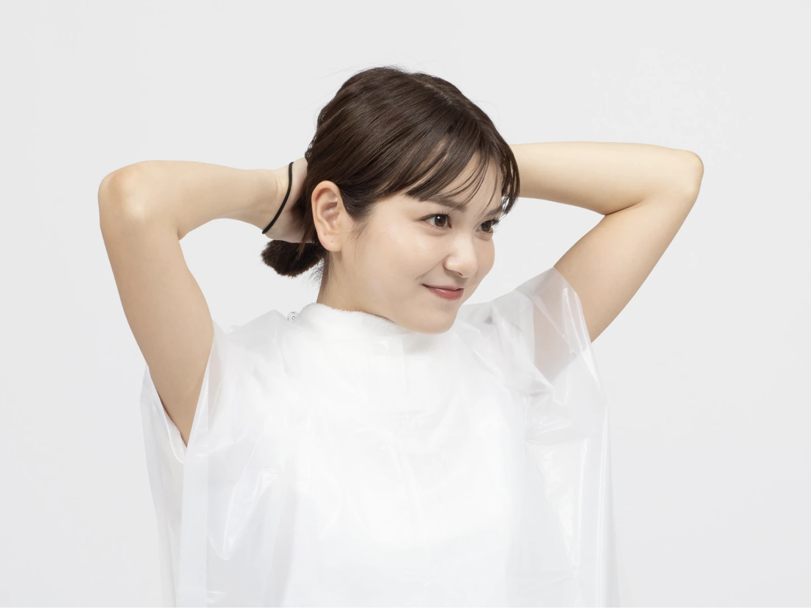 ケープを巻いてヘアゴムで髪を束ねようとしている笑顔の女性