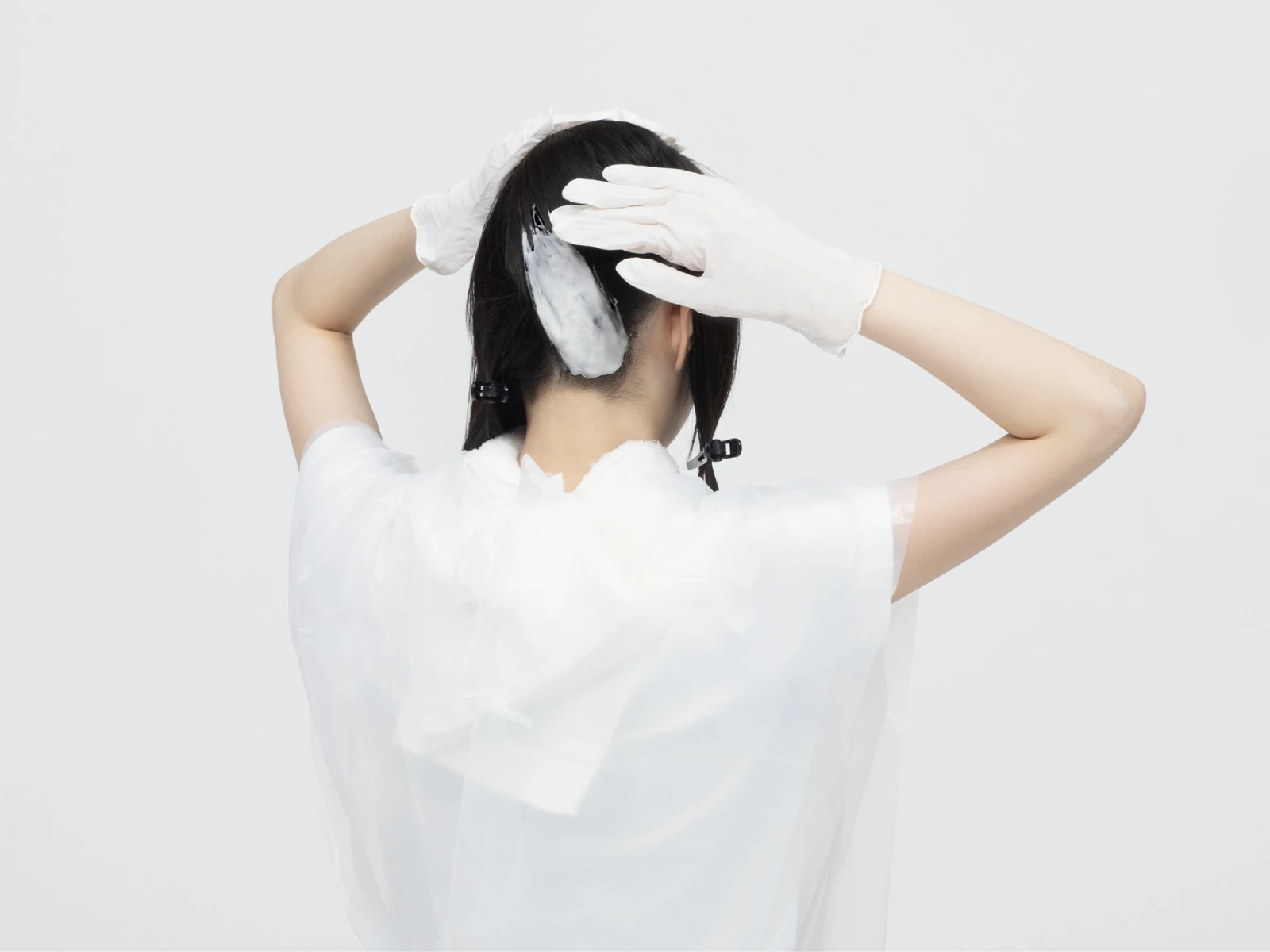 ケープを巻いて手袋をした手でビューティラボを後頭部に塗布している女性の後ろ姿