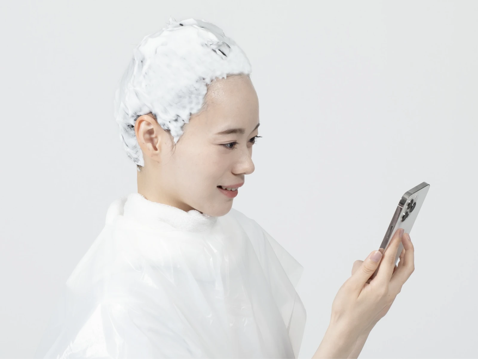 ケープを巻いてビューティラボを髪全体に塗布した状態でスマホを見ている女性