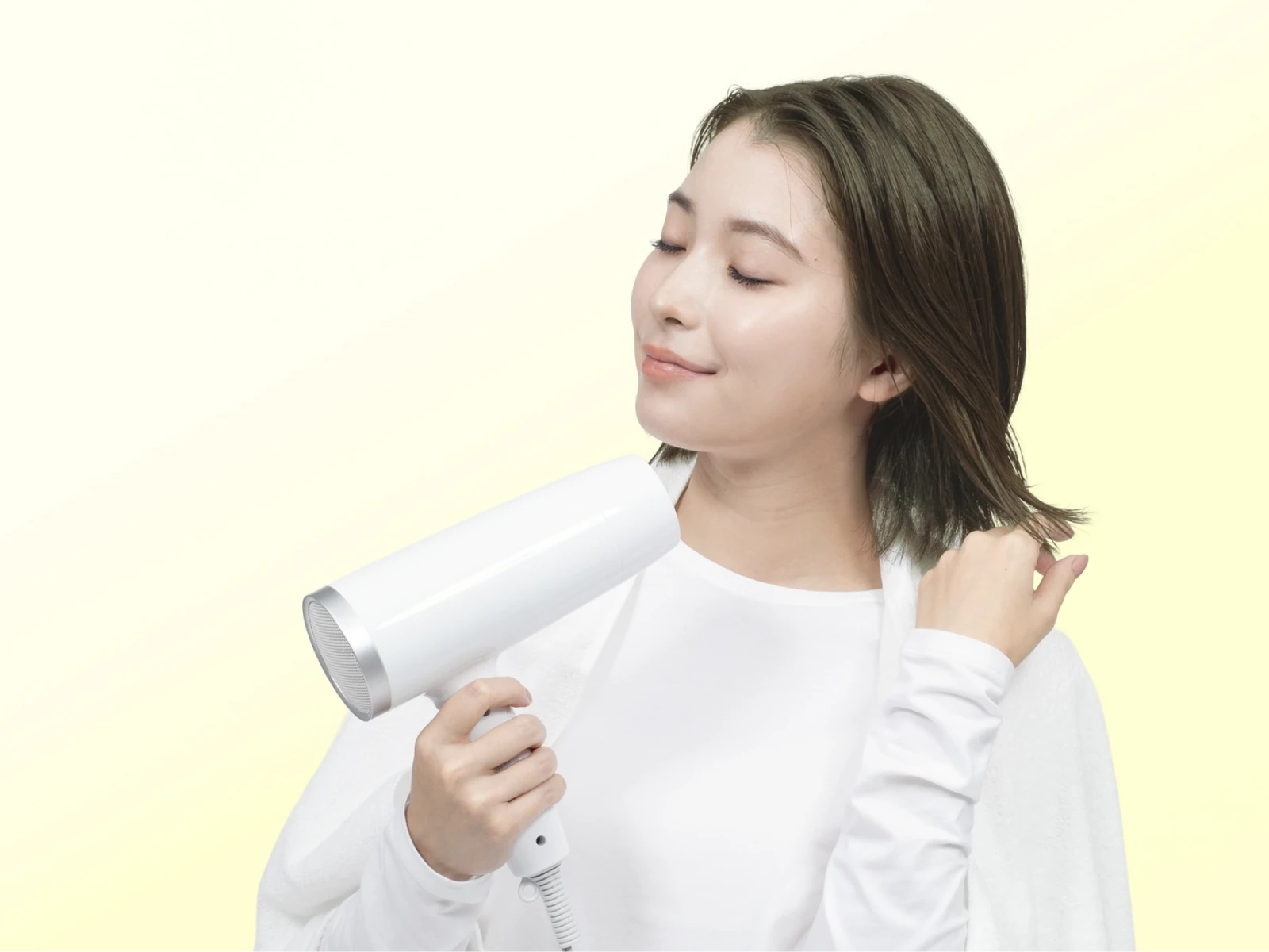 ビューティラボ/ピスタチオアッシュの髪色をして微笑みながら髪にドライヤーをかけている女性